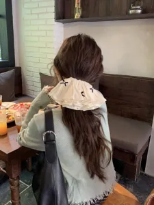 Detailed back view of a woman wearing a cream ruffled bow hair clip in a cozy cafe.