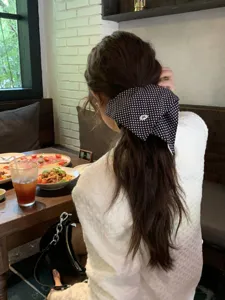 Detail of a black polka dot bow scrunchie worn on a ponytail in a restaurant.