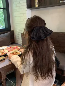 Back view of a model wearing a large black pleated bow hair clip with delicate pearl accents