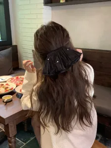 Elegant black pleated bow hair clip with pearl accents worn on long wavy hair