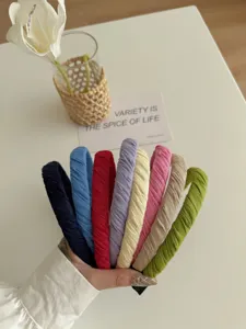 Nahaufnahme einer Hand, die acht bunte, plissierte Stoffstirnbänder auf einem Tisch hält
