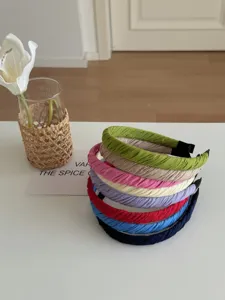 Stapel farbenfroher plissierter Stoffstirnbänder auf weißem Tisch mit Blumendekor.