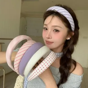 Modèle portant un bandeau rembourré à carreaux et tenant plusieurs serre-têtes colorés