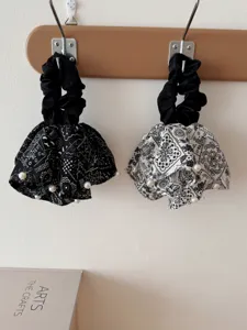 Close-up of black and white vintage paisley fabric scrunchies with pearl accents.