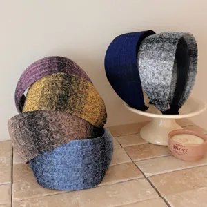 Wide knitted headbands in various colors displayed on a cream pedestal and tile surface