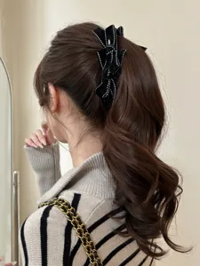 Detailed view of a vintage black velvet bow hair clip with white stitching on a ponytail