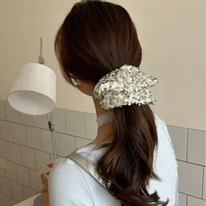 Detailed view of a large silver sequin hair scrunchie worn on a brown low ponytail.
