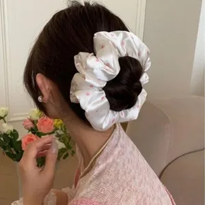 Detailed view of an oversized white satin scrunchie with pink polka dots on a bun