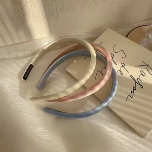 Primer plano de tres diademas finas de satén en beige, rosa y azul sobre tela.