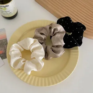 Detail shot of three satin scrunchies with rhinestones on a decorative yellow plate