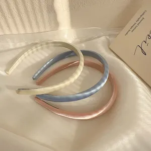 Primer plano de tres elegantes diademas de satén en colores crema, azul y rosa.