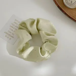 Macro view of a light green satin scrunchie embellished with sparkling rhinestones