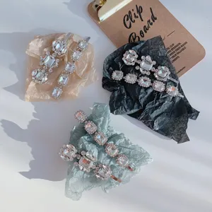 Close-up view of elegant rhinestone hair clips with square and round sparkling crystals.