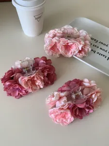 Gros plan de trois élégantes grandes pinces à cheveux en fleurs de tissu roses et bordeaux.