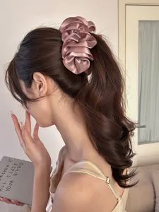 Close-up of a pink satin pleated flower banana hair clip worn on wavy brown hair