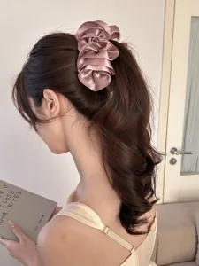 Macro view of a stylish dusty pink satin ruffled flower banana clip worn in a ponytail