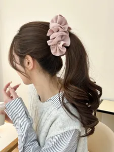 Detail view of a pink pleated fabric banana hair clip styled on a woman's brown ponytail.