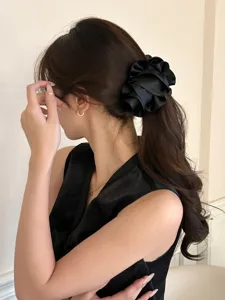 Elegant large black satin ruffled flower banana clip shown worn on wavy brunette hair