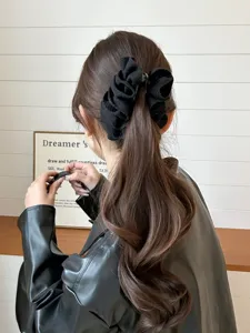 Detail view of an elegant black ruffled banana clip styling a wavy brown ponytail