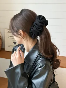 Elegant black ruffled hair scrunchie shown on a woman with long wavy brown hair.