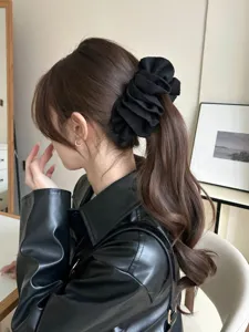 Side view detail of a large black ruffled banana hair clip on a brunette ponytail