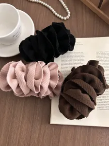 Close-up of three layered fabric flower banana clips in black, pink, and brown.