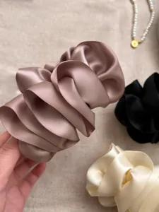 Close-up of pleated satin flower banana clips in mauve, black and cream colors