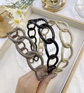 Close-up detail of three glossy plastic chain-link headbands in taupe, black and beige