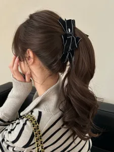Detail showing a black velvet bow hair clip with white stitching on a wavy ponytail.