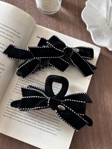 Detailed view of two retro black velvet bow hair clips with white stitching on an open book.
