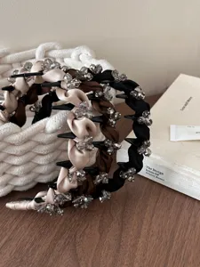 Detail der geflochtenen rutschfesten Haarbänder mit Kristallakzenten in Beige und Braun.