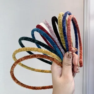 Detail view of various colorful velvet thin headbands with soft pleated texture held in hand