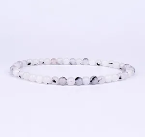 Detailed close-up of white beaded bracelet with natural black and grey stone inclusions.