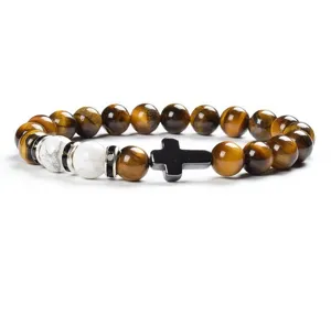 Detail shot of tiger eye stone and white jade beaded bracelet with black cross charm.