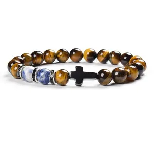Close-up detail of tiger eye stone bead bracelet with black cross pendant and blue stone.