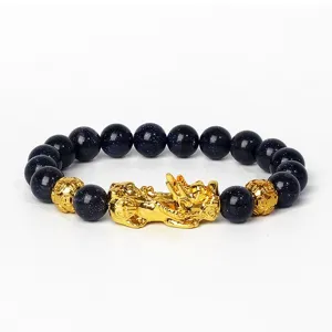 Gros plan détaillé du bracelet en perles de grès bleu avec amulette Pixiu dorée et pièces.