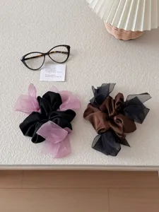 Detail van satijnen scrunchies met transparante mesh strikken in de kleuren zwart en bruin.