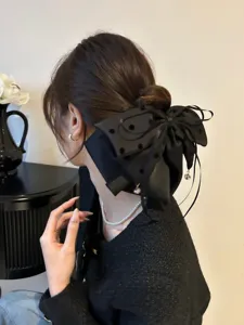 Détail d'une grande pince à cheveux à nœud noir à pois stylisée en chignon bas.