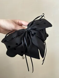 Gros plan sur une grande pince à cheveux nœud en satin noir avec pois en velours.