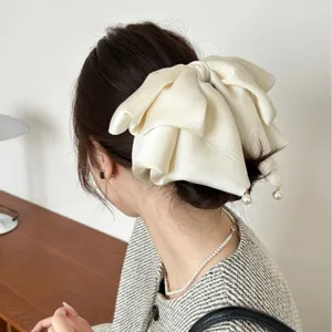Élégante pince à cheveux nœud géant en satin crème avec perles sur un chignon bas.
