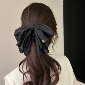 Détail d'une grande pince à cheveux en ruban de satin noir sur une queue de cheval basse