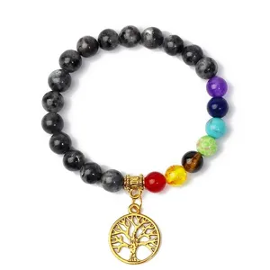 Close-up detail of chakra yoga bracelet with dark beads, colorful stones and tree life pendant.