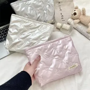 Detailed view of three quilted bow-pattern cosmetic pouches in pink, cream, and silver.