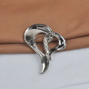 Vista detallada de la parte posterior de un broche de corazón de metal plateado con pin.
