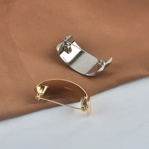Detailed view of gold and silver C-shaped brooches with textured finish and pin back