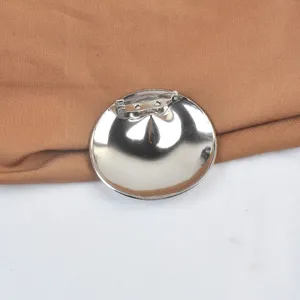 Macro detail of a glossy stainless steel round brooch highlighting the safety pin back