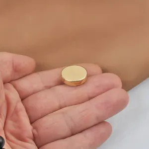 Primer plano de un botón metálico desmontable dorado sin costura sostenido en la mano