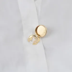Detailansicht eines goldenen runden Hemdknopf-Clips Accessoires auf weißem Stoff.