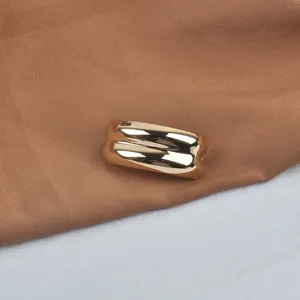 Detailed view of a minimalist gold wavy textured metal brooch with a high-gloss polished finish
