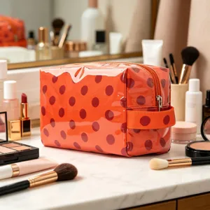 Détail d'une trousse de maquillage en PVC orange brillant à pois rouges sur du marbre